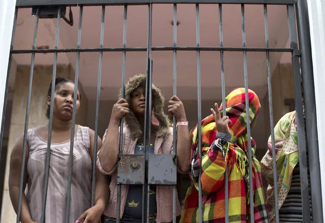 People stand behind a gate at the entrance of an abandoned residential apartment building in the middle class Flamengo neighborhood of Rio de Janeiro, Brazil, Tuesday, April 7, 2015. Squatters invaded the residence that Brazil's one-time richest man was supposed to transform into a luxury hotel ahead of the 2016 Olympic games and are demanding city officials put them into social housing. (Photo by Silvia Izquierdo/AP Photo)