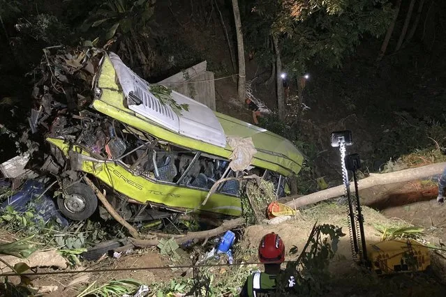 In this photo provided by the Iloilo City Disaster Risk Reduction and Management Office – Urban Search and Rescue Unit, a rescuer rappels down a damaged passenger bus in a ravine at the mountainous Hamtic town, Antique province, central Philippines early Wednesday December 6, 2023. The passenger bus lost control while negotiating a downhill curve and plunged into a deep ravine Tuesday afternoon killing some passengers and injuring others officials said. (Photo by Iloilo City Disaster Risk Reduction and Management Office – Urban Search and Rescue Unit via AP Photo)