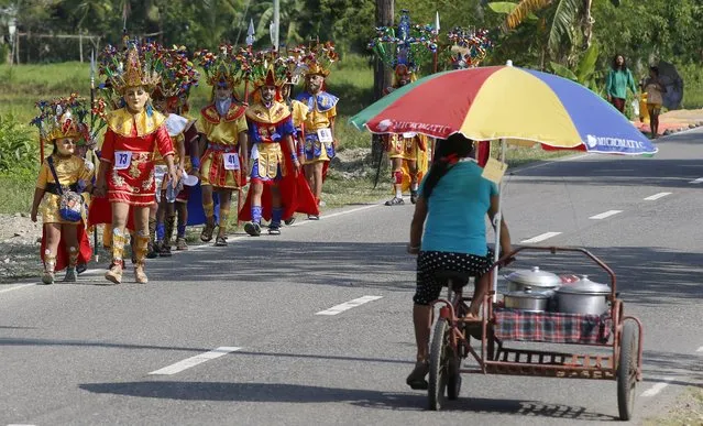 A cooked food peddler cycles past penitents wearing masks and centurion garb, locally called “Morions”, during Holy Week celebrations in Mogpog, Marinduque in central Philippines March 22, 2016. (Photo by Erik De Castro/Reuters)