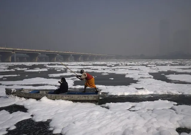 A person takes a boat ride in the Yamuna River, covered by a chemical foam caused by industrial and domestic pollution as the skyline is enveloped in a blanket of toxic smog in New Delhi, India, Wednesday, November 17, 2021. (Photo by Manish Swarup/AP Photo)