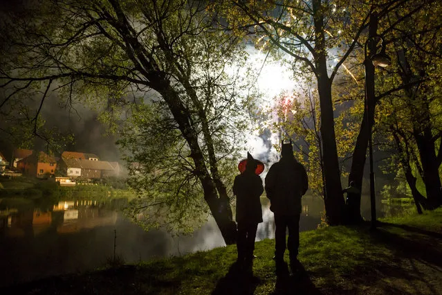 People stand by a lake as they watch fireworks explode over a Walpurgisnacht pagan festival in the town of Stiege, in the Harz mountain region, April 30, 2014. Legend has it that on Walpurgisnacht or May Eve, witches fly their broomsticks to meet the devil at the summit of the Brocken Mountain in Harz. In towns and villages scattered throughout the mountain region, locals make bonfires, dress in devil or witches costumes and dance into the new month of May. Picture taken April 30, 2014. (Photo by Thomas Peter/Reuters)