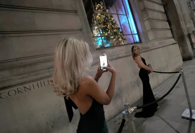 Two women dressed for a party take photos of each other outside a venue in London, Friday, December 17, 2021. On what would normally be one of the busiest times for pubs and restaurants just before Christmas, customer numbers are down in central London due to concerns about the new omicron variant. Friday night in Central London was muted with one bar saying they have 30 customers inside when there should have been 170, with large amounts of cancellations in recent days. (Photo by Alastair Grant/AP Photo)
