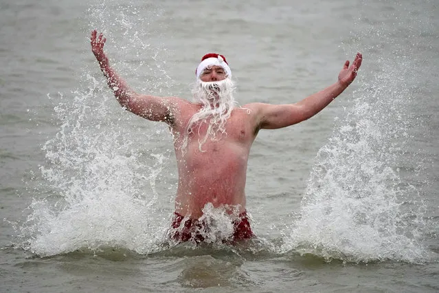 Patrick Corkery wears a santa hat and beard as waves crash over him during a Christmas Day dip at Sandy Cover near Dublin, Ireland, Saturday, December 25, 2021. (Photo by Niall Carson/PA Wire via AP Photo)