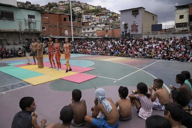 Mothers and children from a soup kitchen watch a Christmas performance at a square in the Mamera neighborhood of Caracas, Venezuela, Thursday, December 16, 2021. (Photo by Ariana Cubillos/AP Photo)