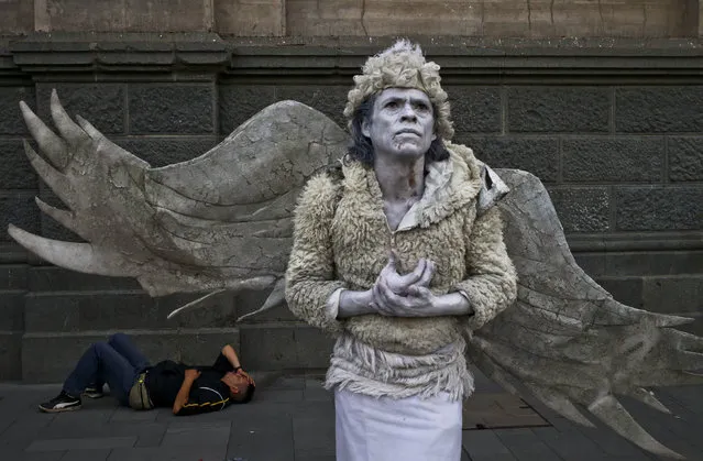 A street performer dressed as an angel holds still, waiting to move only when a pedestrian tips him, as another rests on the ground behind him at the Plaza de Armas in Santiago, Chile, Tuesday, March 7, 2017. The downtown square is the capital's center, hosting municipal offices, the Cathedral, the post office and colorful personalities from artists to street preachers. (Photo by Esteban Felix/AP Photo)
