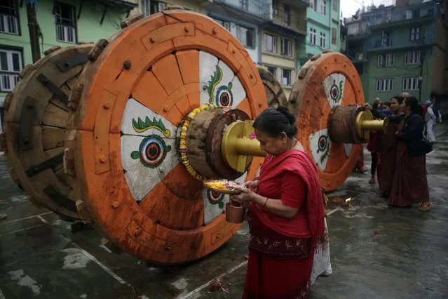 In this April 21, 2017, photo, a Hindu woman performs ritual prayers in front of wheels that will be assembled for the Rato Machindranath Chariot in Lalitpur, Nepal. The chariot built every year is 15-meter (48-foot) tall and based on a chassis that is only as wide as a small truck. The chariot rides high over the heads of people as it sits on four giant wooden wheels decorated with painted eyes. The wooden chariot is built to appease the gods in hopes of being blessed with a good rainfall followed by a bountiful harvest. (Photo by Niranjan Shrestha/AP Photo)