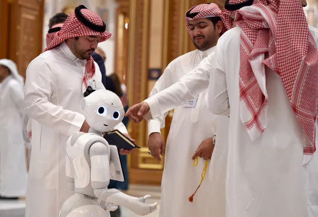 Delegates chat near a robot during the Future Investment Initiative (FII) forum at the King Abdulaziz Conference Centre in Saudi Arabia's capital Riyadh, on October 30, 2019. Top finance moguls and political leaders were expected at a Davos-style Saudi investment summit, in stark contrast to last year when outrage over critic Jamal Khashoggi's murder sparked a mass boycott. Organisers say 300 speakers from over 30 countries, including American officials and heads of global banks and major sovereign wealth funds, are attending the three-day forum. (Photo by Fayez Nureldine/AFP Photo)