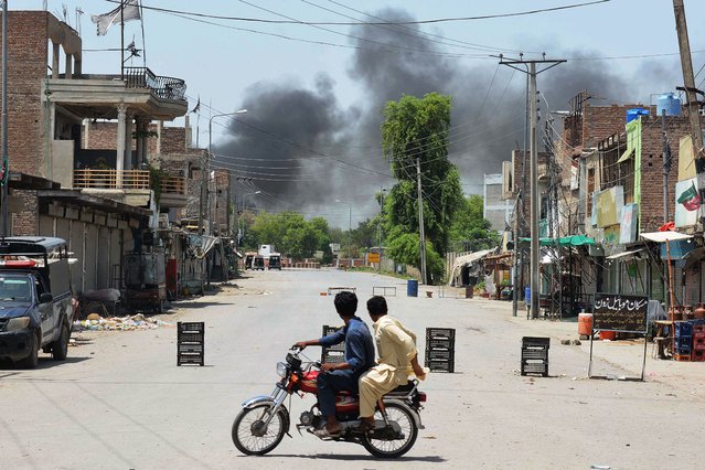 Men riding a bike watch as smoke rises following an explosion allegedly after militants suicide squad attempted to storm an army cantonment that houses military residences and offices in Bannu on July 15, 2024. (Photo by Karim Ullah/AFP Photo)