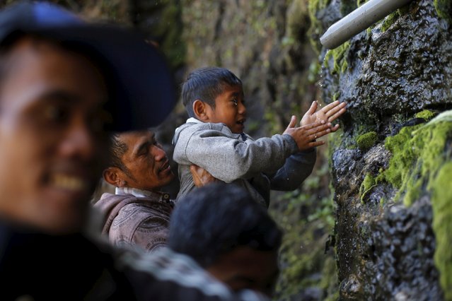 A father holds up his son as they wash their face with holy water from a stream for prayers ahead of the annual Kasada festival at Mount Bromo in Indonesia's East Java province, July 31, 2015. (Photo by Reuters/Beawiharta)