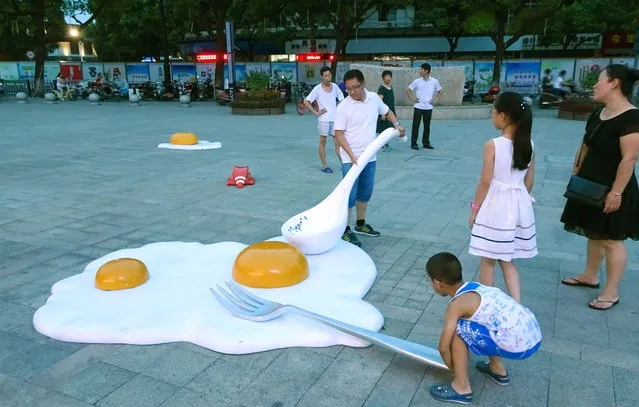 Sunny side up: parents and their children play with giant artworks in the shape of fried eggs, in front of a shopping mall in Shaoxing city, China on August 7, 2017. (Photo by Imaginechina/Rex Features/Shutterstock)