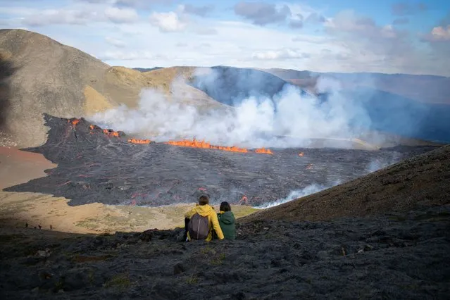 People look at the lava flowing at the scene of the newly erupted volcano at Grindavik, Iceland on August 3, 2022. A volcano erupted on August 3, 2022 in Iceland in a fissure near Reykjavik, the Icelandic Meteorological Office (IMO) said as lava could be seen spewing out of the ground in live images on local media. The eruption was some 40 kilometres (25 miles) from Reykjavik, near the site of the Mount Fagradalsfjall volcano that erupted for six months in March-September 2021, mesmerising tourists and spectators who flocked to the scene. (Photo by Jeremie Richard/AFP Photo)