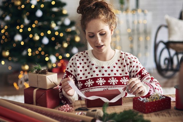 Woman tying ribbon on Christmas present. (Photo by Gpointstudio/Getty Images)