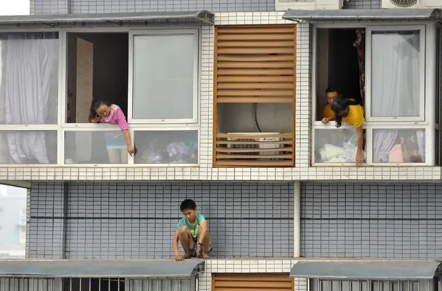 A twelve-year-old boy sits outside a window of his eleventh-floor apartment as his relatives try to ask him to come back back inside, in Yibin, Sichuan province, September 8, 2014. The boy was afraid of being punished by his mother for not finishing his homework on time. After two hours' standoff, he was persuaded by police and family members to come inside. (Photo by Reuters/Stringer)