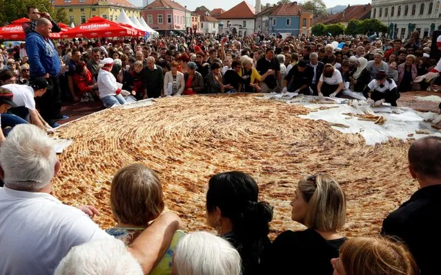 Bosnian chefs and their apprentices, cut the World's largest minced meat pie, known as “burek”, on the central square in Tuzla, on October 14, 2017. This pie was made as an attempt at the Guinness record for the largest burek. It weighed 650 kilograms, was made from 1.5 kms of hand rolled dough and the final product measured 6.5 meters in diameter. After the public presentation at the square, the pie was cut up in 4.500 portions and distributed to several thousands of citizens of Tuzla, who gathered at the square to witness the ceremony. (Photo by Elvis Barukcic/AFP Photo)