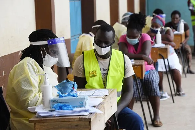 A health care worker (L) writes on a sample of a specimen bottle while a resident of Eastleigh waits in the queue to be tested during a mass testing exercise for  the COVID-19 coronavirus in Nairobi on May 20, 2020. (Photo by Simon Maina/AFP Photo)