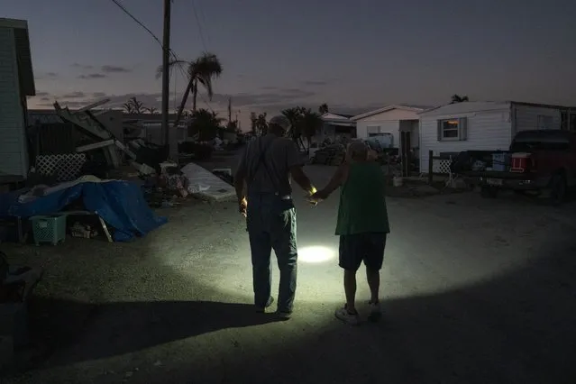 Charlie Whitehead, left, helps his 84-year-old neighbor Leslie Pickett down the street of their mobile home community on October 7, 2022 in San Carlos Island, Florida. Pickett, who suffers from dementia, and his wife, Pat, 83, weathered Hurricane Ian in their mobile home, which was flooded by the storm surge and left them floating inside. Whitehead, who describes himself as a lost son of theirs, has been helping them and has erected a tent where they now sleep. The electricity in their neighborhood, one of the hardest hit by Ian, has been out since the storm over a week ago. (Photo by Michael Robinson Chavez/The Washington Post)