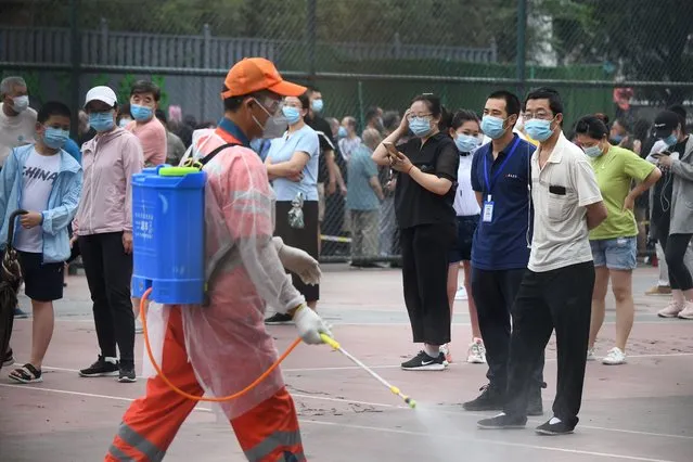 A worker sprays disinfectant as people wearing face masks gather at an outdoor area to take a swab test during mass testing for the COVID-19 coronavirus in Beijing on June 23, 2020. (Photo by Noel Celis/AFP Photo)