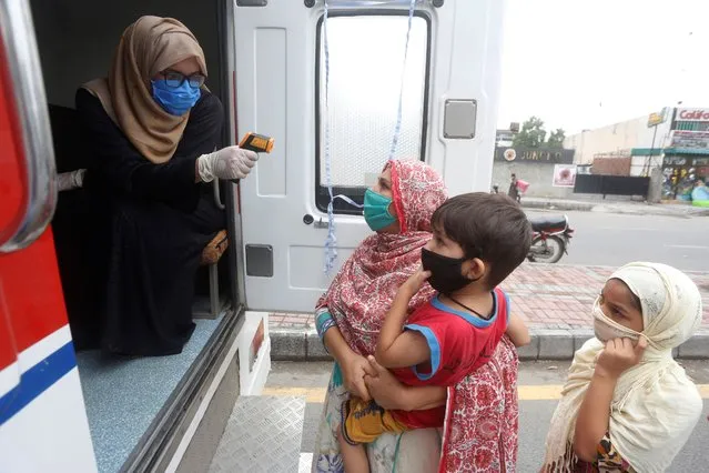 A health worker checks the body temperature of a woman at a mobile screening unit set up to control the spread of the coronavirus, in Lahore, Pakistan, Thursday, June 25, 2020. (Photo by K.M. Chaudhry/AP Photo)