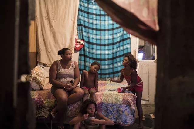 In this September 14, 2017 photo, Luciana Bastos sits in her room with her girls as they watch television inside a building that used to house the Brazilian Institute of Geography and Statistics (IBGE), now occupied by hundreds of people in the Mangueira slum of Rio de Janeiro, Brazil. Bastos, 30, recently moved here with her husband and two daughters after they both lost their jobs and couldn’t make rent. (Photo by Felipe Dana/AP Photo)