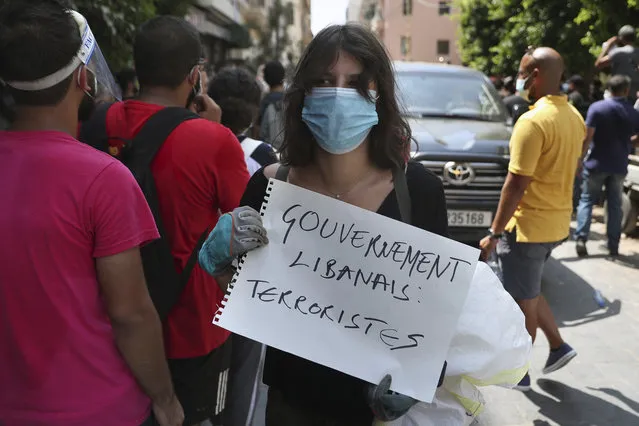 A woman holds a placard in French that reads, “Lebanese government terrorists”, next to a convoy of French President Emmanuel Macron as he visits the Gemayzeh neighborhood, which suffered extensive damage from an explosion on Tuesday that hit the seaport of Beirut, Lebanon, Thursday, August 6, 2020. (Photo by Bilal Hussein/AP Photo)