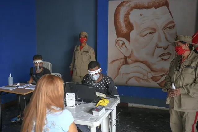 Members of the Venezuelan Electoral Council, sitting, wear face masks and shields amid the spread of the new coronavirus at a validation center, featuring a drawing of late President Hugo Chavez, to certify the authenticity of voter data in Caracas, Venezuela, Saturday, July 25, 2020. The legislative election is scheduled for Dec. 6 and thus far the opposition has indicated it will not participate. (Photo by Matias Delacroix/AP Photo)