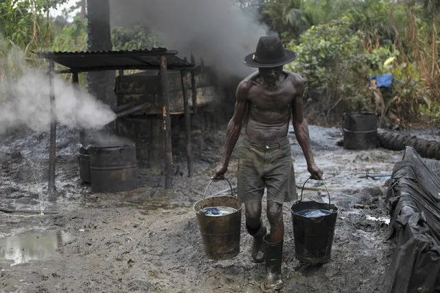 Ebiowei, 48, carries refined oil in buckets at an illegal oil refinery site near river Nun in Nigeria's oil state of Bayelsa November 27, 2012. Thousands of people in Nigeria engage in a practice known locally as 'oil bunkering' - hacking into pipelines to steal crude then refining it or selling it abroad. (Photo by Akintunde Akinleye/Reuters)