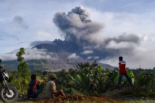 Villagers watch the eruption of Mount Sinabung as seen from Karo, North Sumatra on August 13, 2020. Indonesia's Mount Sinabung erupted again on August 13 with a string of blasts that sent plumes of ash two kilometres (1.2 miles) into sky, triggering a flight warning and fears of lava flows. (Photo by Anto Sembiring/AFP Photo)