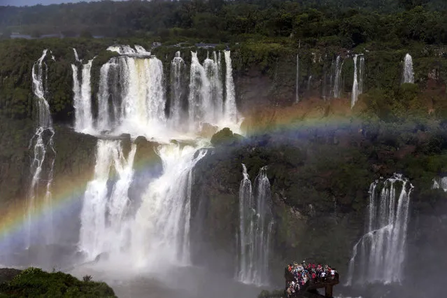 A rainbow forms over tourists visiting Iguazu Falls in Foz do Iguazu, Brazil, on March 15, 2015. The waterfalls, on the border of Argentina and Brazil, are part of the Guarani Aquifer, one of the world's major underground reserves of fresh water. (Photo by Jorge Saenz/AP Photo)