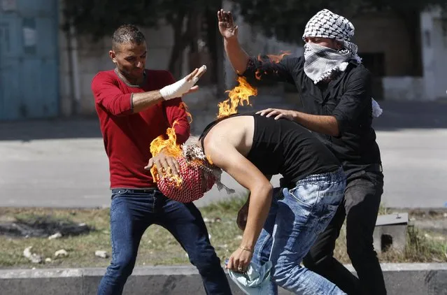 Palestinian protesters put out a fire burning on a compatriot, caused by a molotov cocktail which he was trying to hurl at Israeli troops during clashes in the West Bank city of Hebron October 13, 2015. (Photo by Mussa Qawasma/Reuters)