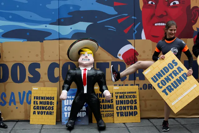 A participant holds a sign as she plays with a pinata depicting U.S. Republican presidential nominee Donald Trump in front of a wall with a caricature of him during a campaign encouraging U.S. citizens in Mexico to register to vote against Trump, in Mexico City, Mexico September 25, 2016. The sign reads: “United against Trump”. (Photo by Carlos Jasso/Reuters)