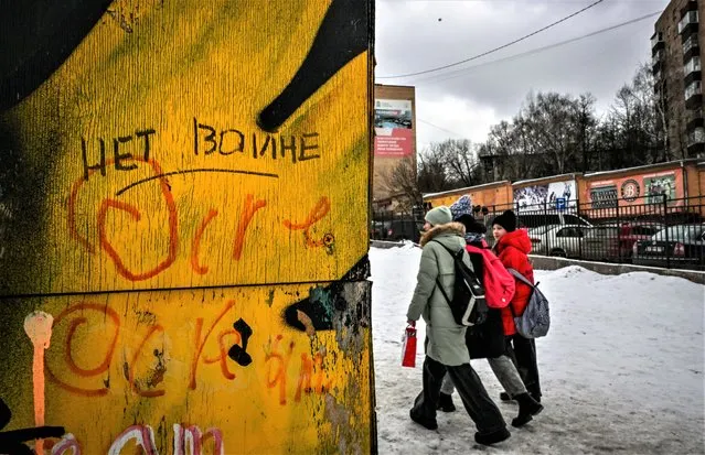 Pedestrians walk past a wall with graffiti and the inscription reading “No to war” left on a wall in the town of Chekhov some 75 kilometres outside Moscow on February 11, 2023. Despite strict government censorship and the threat of jail, residents of Russia's capital are finding subtle ways to express alarm and dissent over the Kremlin's year-long offensive in Ukraine. The messages are barely visible but omnipresent throughout Moscow, scrawled and graffitied on walls, pasted as stickers on drain pipes or carved into the wood of benches. (Photo by Yuri Kadobnov/AFP Photo)