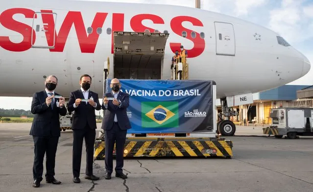 Sao Paulo Governor Joao Doria (C), Sao Paulo state Health Secretary Dr. Jean Gorinchteyn (L), and Butantan Institute Director Dimas Covas (R), pose for photos next to a container carrying doses of the CoronaVac vaccine after it was unloaded from a cargo plane that arrived from China at Guarulhos International Airport in Guarulhos, near Sao Paulo, Brazil, on December 03, 2020. Brazil received this Thursday the second lot with 600 liters of the CoronaVac vaccine, developed by the Chinese laboratory Sinovac Biotech. (Photo by Nelson Almeida/AFP Photo)