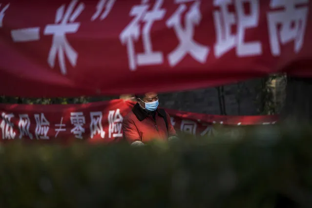 A man wearing a face mask to help curb the spread of the coronavirus walks by propaganda banners displaying coronavirus precaution messages along a neighborhood alley in Beijing, Sunday, November 29, 2020. (Photo by Andy Wong/AP Photo)