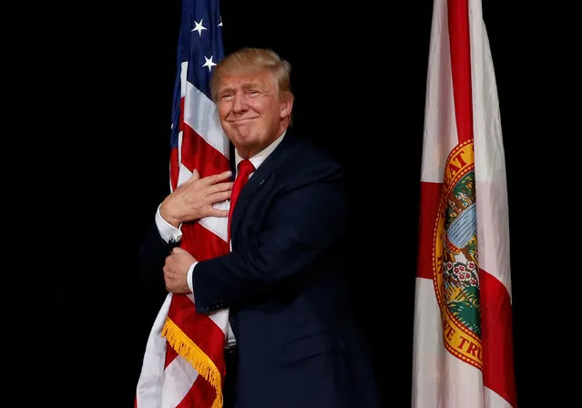 Republican U.S. presidential nominee Donald Trump hugs a U.S. flag as he comes onstage to rally with supporters in Tampa, Florida, U.S. October 24, 2016. (Photo by Jonathan Ernst/Reuters)