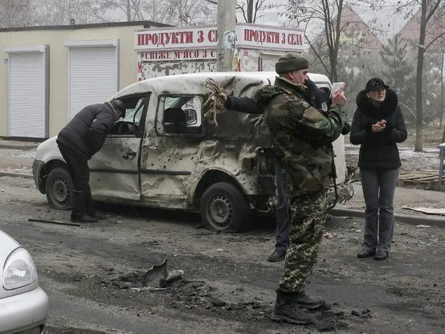 A Ukrainian serviceman and local residents inspect a damaged car after a shelling in the eastern Ukrainian city of Mariupol, 24 January 2015. (Photo by Sergey Vaganov/EPA)