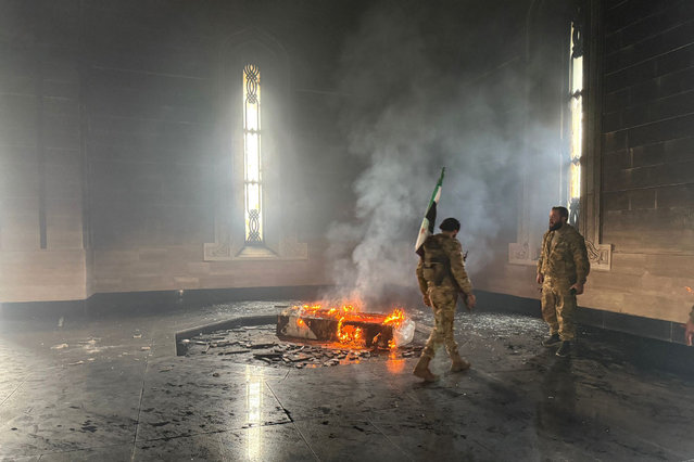 Rebel fighters stand next to the burning gravesite of Syria's late president Hafez al-Assad at his mausoleum in the family's ancestral village of Qardaha in the western Latakia province on December 11, 2024, after it was stormed by opposition factions. The father and predecessor of Syria's ousted president Bashar al-Assad died in 2000. (Photo by Aaref Watad/AFP Photo)