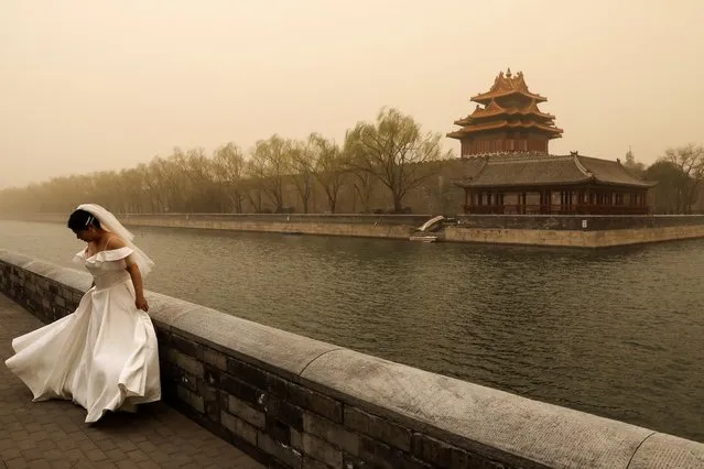 A woman in bridal gown adjusts herself during a wedding photoshoot near the Forbidden City, as the city is hit by sandstorm, in Beijing, China on March 15, 2021. (Photo by Tingshu Wang/Reuters)