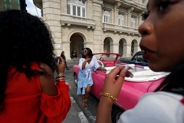 U.S. tourists take photographs next to vintage cars in Havana, Cuba, July 16, 2018. (Photo by Reuters/Stringer)
