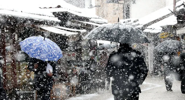 People walk under a heavy snowfall on a street in Sarajevo, Bosnia and Herzegovina, 15 March 2021. Meteorologists forecast snowy weather with low temperatures to continue in the upcoming days. (Photo by Fehim Demir/EPA/EFE)