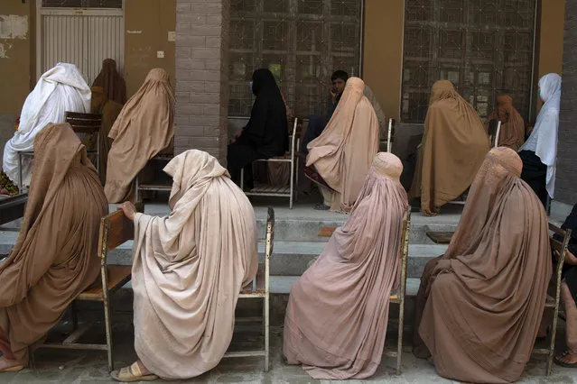 Women wearing a burqa sit in a queue to collect financial assistance through the Ehsaas Emergency Cash programme for families in need, ahead of the Holy month of Ramadan in Peshawar on April 12, 2021. (Photo by Abdul Majeed/AFP Photo)