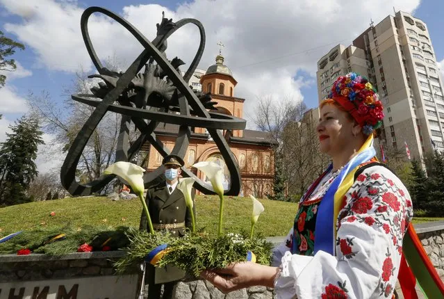 A woman in a Ukrainian folk costume lays flowers to the Chernobyl victims monument in capital Kyiv, Ukraine, Monday, April 26, 2021. April 26 marks the 35th anniversary of the Chernobyl nuclear disaster. A reactor at the Chernobyl nuclear power plant exploded on April 26, 1986, leading to an explosion and the subsequent fire spewed a radioactive plume over much of northern Europe. (Photo by Efrem Lukatsky/AP Photo)
