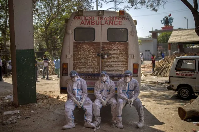 Exhausted workers, who bring dead bodies for cremation, sit on the rear step of an ambulance inside a crematorium, in New Delhi, India, Saturday, April 24, 2021. Delhi has been cremating so many bodies of coronavirus victims that authorities are getting requests to start cutting down trees in city parks, as a second record surge has brought India's tattered healthcare system to its knees. (Photo by Altaf Qadri/AP Photo)