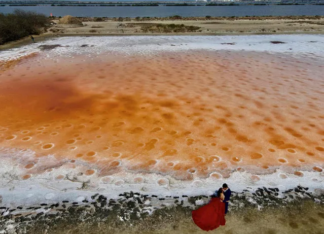 An aerial view shows a wedding couple kissing as they pose for photographs next to a pink coloured salt field, caused by no rain, in Tainan, Taiwan on April 21, 2021. (Photo by Sam Yeh/AFP Photo)