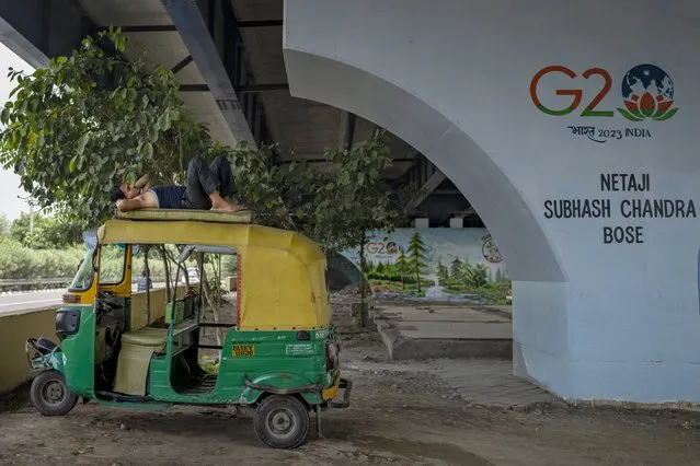 An auto rickshaw driver sleeps on the roof of his rickshaw under an elevated road next to a G20 logo in New Delhi, India, Thursday, September, 7, 2023. Leaders of the Group of 20 leading rich and developing countries are gathering in New Delhi this weekend for their annual summit. (Photo by Altaf Qadri/AP Photo)