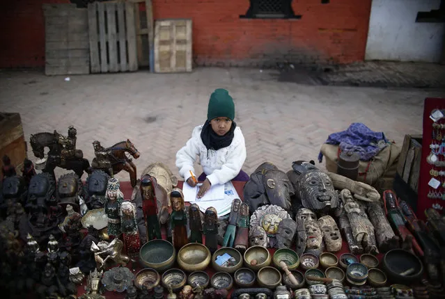 A girl completes her homework sitting at her father's stall on a street of Bashantapur Durbar Square in Kathmandu, Nepal February 2, 2016. (Photo by Navesh Chitrakar/Reuters)