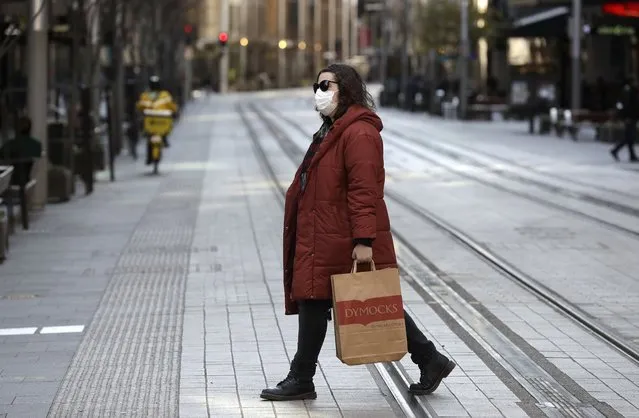 A woman crosses a normally busy street in Sydney, Wednesday, July 7, 2021. Sydney's two-week lockdown has been extended for another week due to the vulnerability of an Australia population largely unvaccinated against COVID-19, officials said. (Photo by Rick Rycroft/AP Photo)
