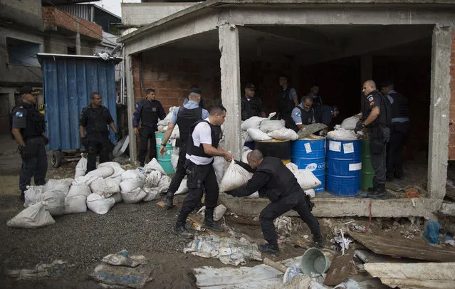 Police officers make a barricade out of cement filled steel drums and sand bags while building a checkpoint at the Alemao slum complex as part of a security reinforcement by the UPP (Police Pacification Unit) in Rio de Janeiro, Brazil, Tuesday, April 7, 2015. (Photo by Leo Correa/AP Photo)