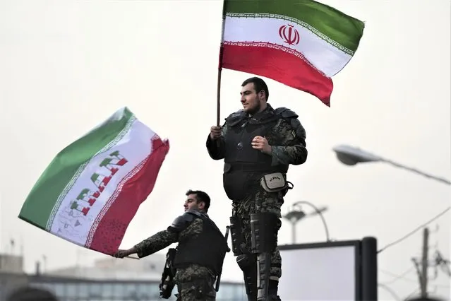 Two anti-riot police officers wave the Iranian flags during a street celebration after Iran defeated Wales in Qatar's World Cup, at Sadeghieh Sq. in Tehran, Iran, Friday, November 25, 2022. Iran's political turmoil has cast a shadow over Iran's matches at the World Cup, spurring tension between those who back the team and those who accuse players of not doing enough to support the protests that started Sept. 16 over the death of a 22-year-old woman in the custody of the morality police. (Photo by Vahid Salemi/AP Photo)