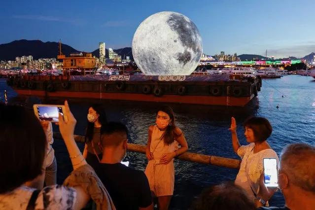 People pose in front of a giant moon-shaped balloon ahead of Mid-Autumn Festival, in Hong Kong, China on September 20, 2021. (Photo by Tyrone Siu/Reuters)