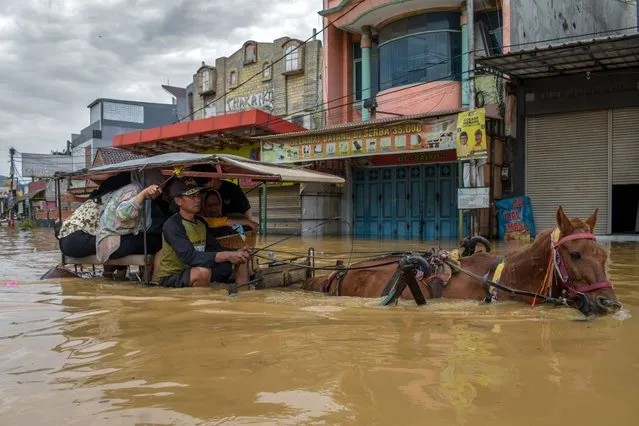 Residents evacuate using a horse-drawn carriage in the flooded town of Dayeuhkolot in Bandung on January 12, 2024, after a river overflowed due to heavy rain. (Photo by Timur Matahari/AFP Photo)